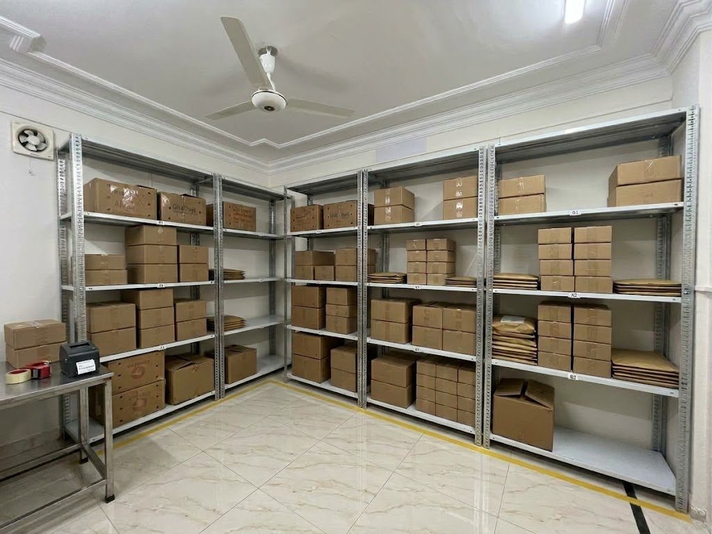 RapidXpk warehouse in Karachi: steel shelves of brand cartons, a packing table and a label printer